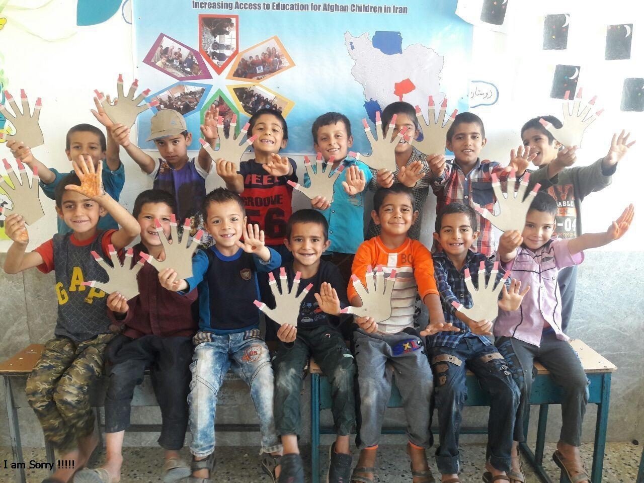 A group of smiling Afghan boys holding up paper hand cut-outs in a classroom